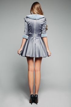 Back view of tall model wearing pretty grey dress decorated with fur on collar and sleeves. Wearing black high heels. Isolate.