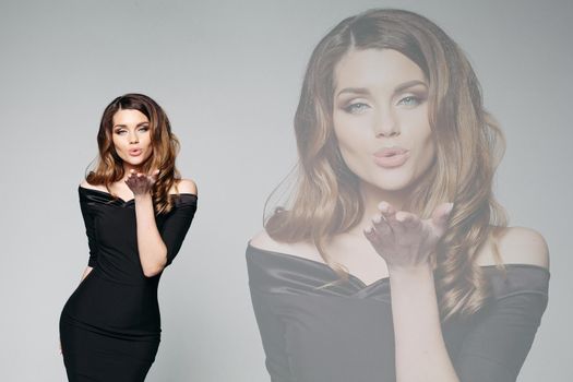 Effect of two differnet views on one seductive brunette woman with curly hair, who sanding and blowing kiss at camera. Sensuality girl with plump lips wearing in black dress posing in gray studio.