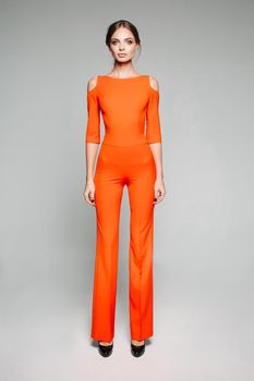 Full length studio portrait of model in high heels and orange overall with bare shoulders. Isolate on grey.