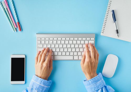 Bright blue modern desk. Top view. Distance education. Copy space, mock up. Freelancer, Digital nomad concept. Keyboard and mobile phone on table