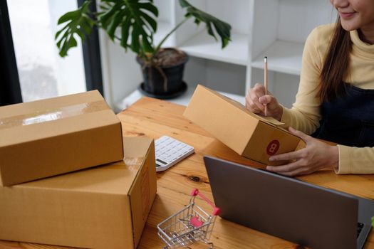 Starting small businesses SME owners female entrepreneurs writing address on receipt box and check online orders to prepare to pack the boxes, sell to customers, sme business ideas online.