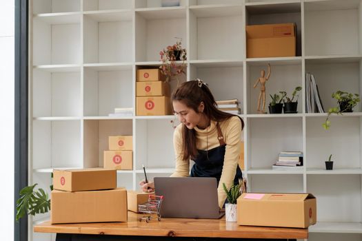 Start up small business entrepreneur SME or freelance asian woman using laptop with box, Young success Asian woman with her hand lift up , online marketing packaging box and delivery, SME concept.