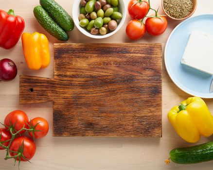 Vegetables around wooden cutting board on kitchen table. Greek salad horiatiki. Top view, copy space. Menu, recipe, mock up. Food ingredient background.