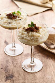 Risotto with mushrooms in wine glass. Unconventional unusual serving. Rice porridge with mushrooms. Wooden old table. Hot dish in glass bowl. Side view, vertical