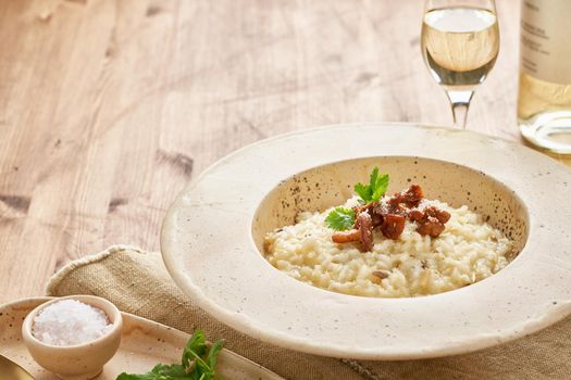 Risoto with chanterelle mushrooms in large plate. Traditional italian dish. Wooden old table, spoons, napkin. Classic hot dish of rice, cheese and wine. Side view, copy space