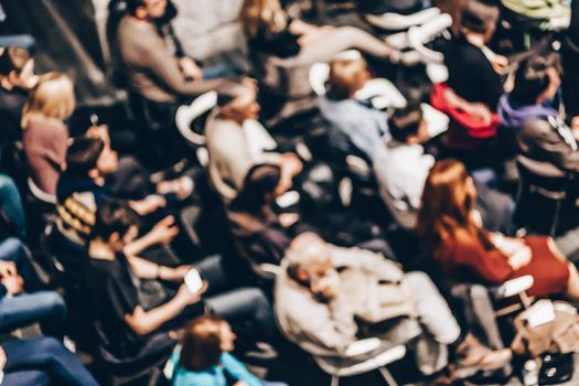 Abowe shot of blured audience in conference hall. Presentation in lecture hall at university workshop. Rear view of unrecognized participant in audience. Scientific conference event.