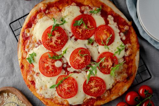 Rustic Italian homemade Pizza Dough margherita topped with pizza sauce from canned tomatoes, mozzarella cheese and arugula on dark linen textile tablecloth
