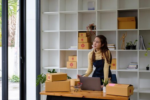 Start up small business entrepreneur SME or freelance asian woman using laptop with box, Young success Asian woman with her hand lift up , online marketing packaging box and delivery, SME concept.