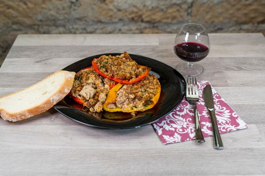 plate of peppers au gratin on wooden table set with cutlery and glass of wine