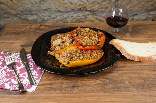 plate peppers au gratin on wooden table with bread cutlery and glass of red wine