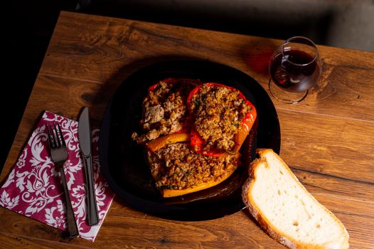 plate peppers au gratin on wooden table with bread cutlery and glass of red wine