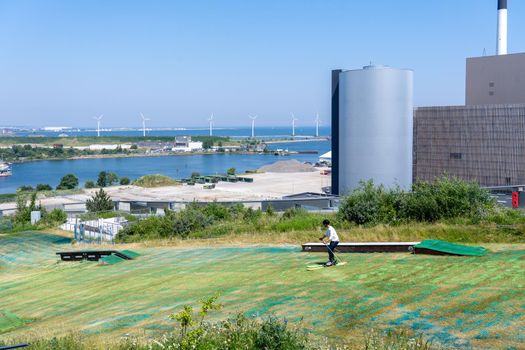 Copenhagen, Denmark - June 18, 2021: Young man skiing down the artificial slope on top of Amager Bakke, a waste to power plant.