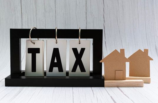 Tax text on paper stand black frame with house model on white wooden background. Property tax and tax time concept