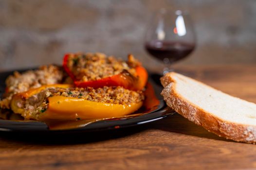 plate peppers au gratin on wooden table with bread cutlery and glass of red wine