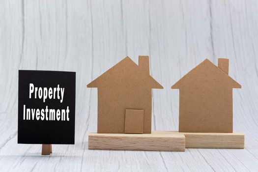Investment property text on black note with house model on white wooden background. Concept for real estate property investment.