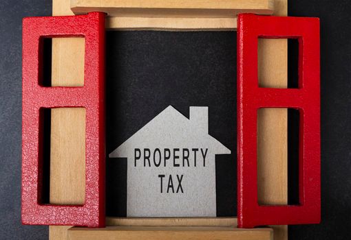 Property tax text on paper house model and in window frame on dark background. Real estate property tax and investment concept.