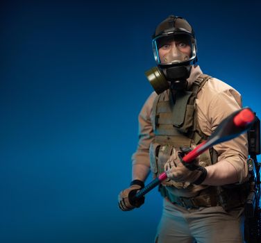 a soldier in military clothes with a bulletproof vest in a gas mask is holding a red fire axe in his hands in fright