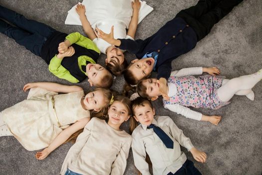 Boys and girls in circle. Happy children having fun. kids lay down together. Happy children lying on the floor in a circle with hands. Top view. Group of children beautiful smile lying on the floor.