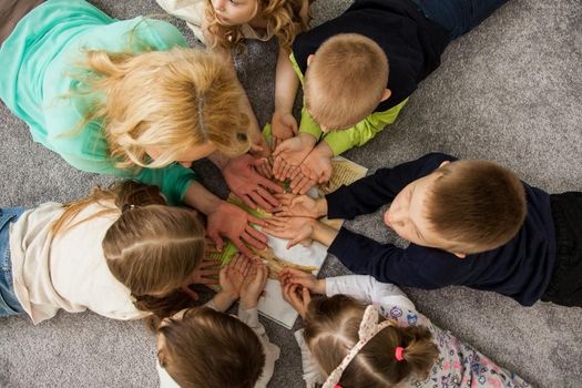 Boys and girls in circle. Happy children having fun. kids lay down together. Happy children lying on the floor in a circle with hands. Top view. Group of children beautiful smile lying on the floor.