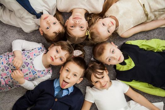 Boys and girls in circle. Happy children having fun. kids lay down together. Happy children lying on the floor in a circle with hands. Top view. Group of children beautiful smile lying on the floor.
