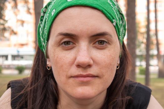 Close-up portrait. Beautiful young woman without makeup in a black T-shirt and a green headdress from the sun on a sunny summer day outdoors. Sunlight