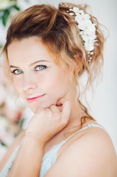 Gorgeous and beautiful woman with curly hairstyle with flowers and blue eyes touching face by hand. Pretty and sweet female wearing in lingerie smiling at camera. Beauty concept.