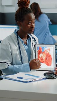 Doctor showing tablet with heart figure for cardiology checkup to patient at consultation. Young parent looking at device with organ for cardiovascular and blood flow healthcare.