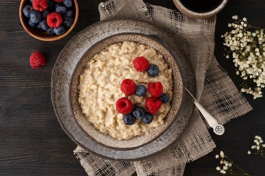 Oatmeal rustic porridge with blueberry, raspberries in ceramic vintage bowl, dash diet with berries, wooden dark brown background, top view close up. Healthy diet breakfast