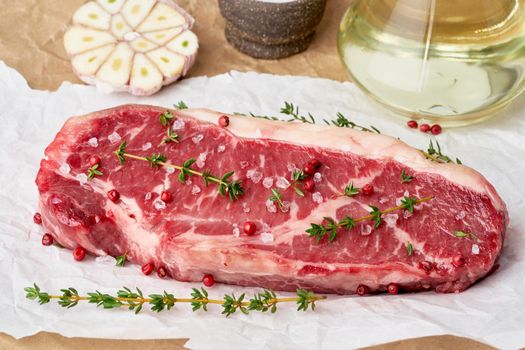 Big whole piece of raw beef meat, striploin on white parchment paper on craft background, zero waste packing. Seasoning steak with salt, side view, close up, banner
