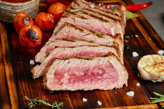Keto ketogenic diet grilled fried beef steak, striploin on cutting board on dark brown table. Paleo food recipe with grilled fried chopped piece of meat, papper, side view, close up