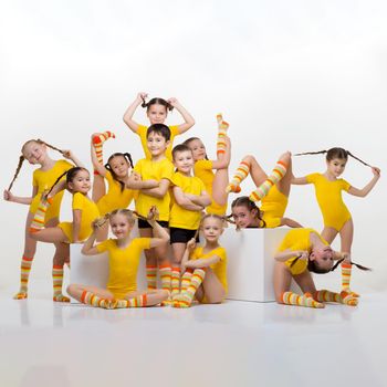 Happy little gymnasts or acrobats posing in studio. Group of cute little boys and girls with pigtails wearing yellow sportswear doing acrobatic stunts against white background