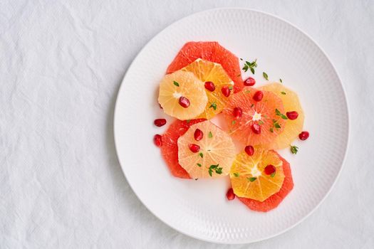 Bright mix of citrus fruits, vertical. Salad of mix sliced round slices of red and white grapefruit sprinkled with pomegranate seeds on white plate. Copy space