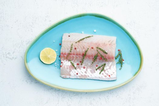 Fillet of raw white walleye fish on a blue plate on a white background. Whole piece of fresh fish with herbs and lemon. Top view