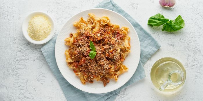 Pasta Bolognese campanelle with mincemeat and tomato sauce, parmesan cheese, basil. Italian dinner, white table. Top view, close up, long banner