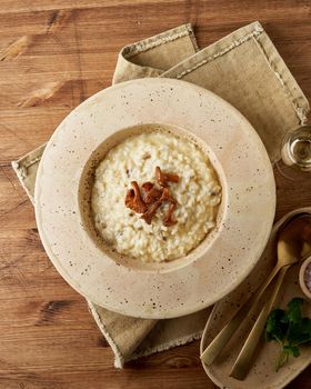 Risoto with chanterelle mushrooms in large plate. Traditional italian dish. Wooden old table, spoons, napkin. Classic hot dish of rice, cheese and wine. Top view, vertical