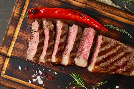 Keto ketogenic diet grilled fried beef steak, striploin on cutting board on dark brown table. Paleo food recipe with grilled fried chopped piece of meat, papper, top view