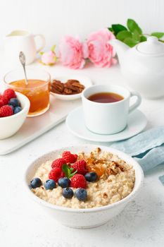 Oatmeal porridge with blueberry, raspberries, jam and nuts in white bowl, dash diet with berries, white background, side view, vertical. Healthy diet breakfast