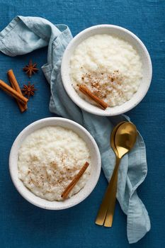 Rice pudding. French milk rice dessert. Healthy Vegan diet breakfast with coconut milk, cinnamon. Blue linen textile. Dark background. Top view, vertical