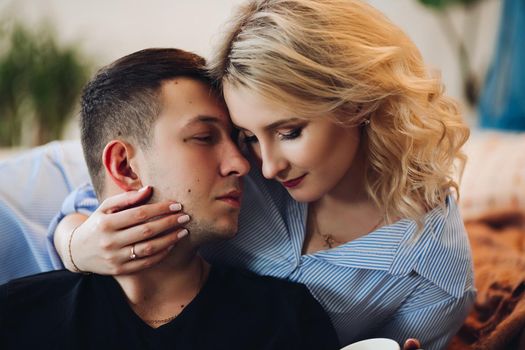 Close up of young happy couple in stylish bedroom embracing each other with closed eyes. Beautiful blonde girlfriend with handsome boyfriend touching face by face.