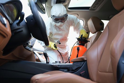 Portrait of worker cleanse car interior with spray disinfectant in container. Disinfect automobile upholstery from germs and virus. Covid prevent concept