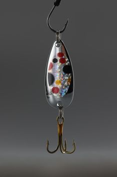 Close-up of fishing hook, sharp tip of hook, equipment to catch fish in lake or river water. Fishing lure wobbler on grey background. Hunt, fishing concept