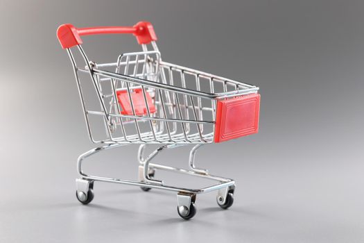 Close-up of empty shopping cart against grey background, single miniature model of container to collect products. Shopping, grocery, food, storage concept