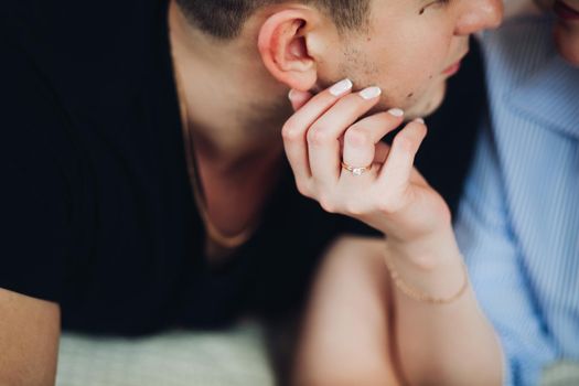 Close up of sensuality girlfriend touching face skin of her boyfriend and looking in his eyes. Couple lying on bed and kissing. Romantic moments, concept of relationship.