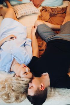 Above view of positivity couple laying together on back and happy smiling. Family spanding time together at home. Blonde woman in blue shirt and man in black t shirt. Concept of love and happiness.