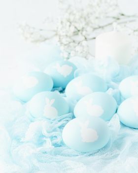 Easter. Holiday. Light white background, gentle pastel colors. Blue eggs with image of rabbit in basket. Flowers in background, side view, vertical