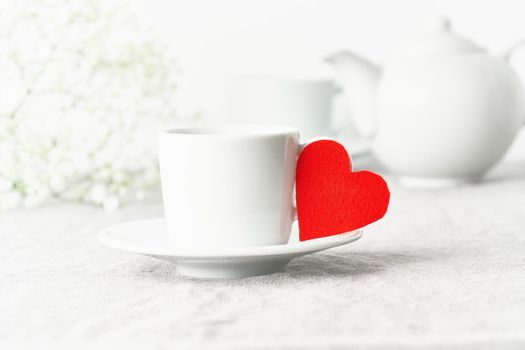 Valentine's Day. Morning breakfast for two with tea and flowers. Red felt heart is symbol of lovers. Light white tender pastel background. Scandinavian minimalism. Side view, copy space