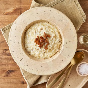 Risoto with chanterelle mushrooms in large plate. Traditional italian dish. Wooden old table, spoons, napkin. Classic hot dish of rice, cheese and wine. Top view