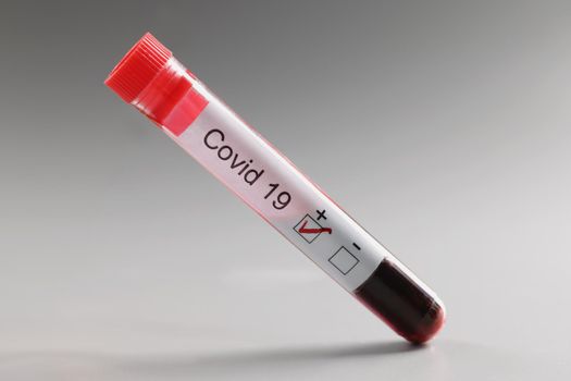 Close-up of test tube with coronavirus positive blood result on grey background. New coronavirus infection, virus spread. Medicine, healthcare, ill concept