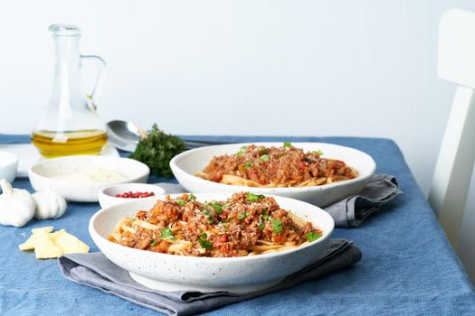 Pasta Bolognese Linguine with mincemeat and tomatoes. Italian dinner for two at the table, dark blue tablecloth, chair, homeliness. Side view