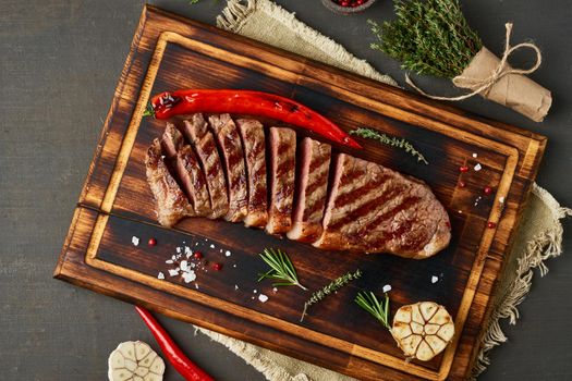 Keto ketogenic diet beef steak, well done grilled fried striploin on cutting board on dark brown table. Paleo food recipe with chopped piece of meat, top view, copy space